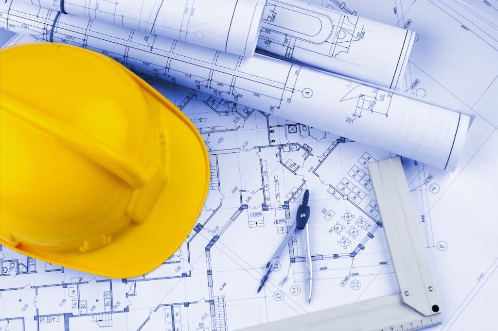 Capacete amarelo e instrumentos de desenho sobre plantas arquitetônicas