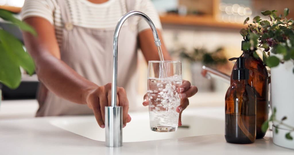 Pessoa enchendo um copo com água filtrada em uma torneira moderna de cozinha